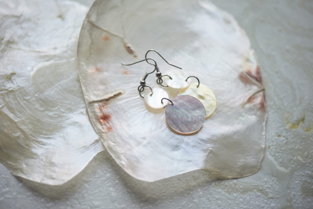 Sea collection on grey marble background.Seashell and mother-of-pearl earrings. Summer jewelry.Mother-of-pearl plates and pearl earrings.